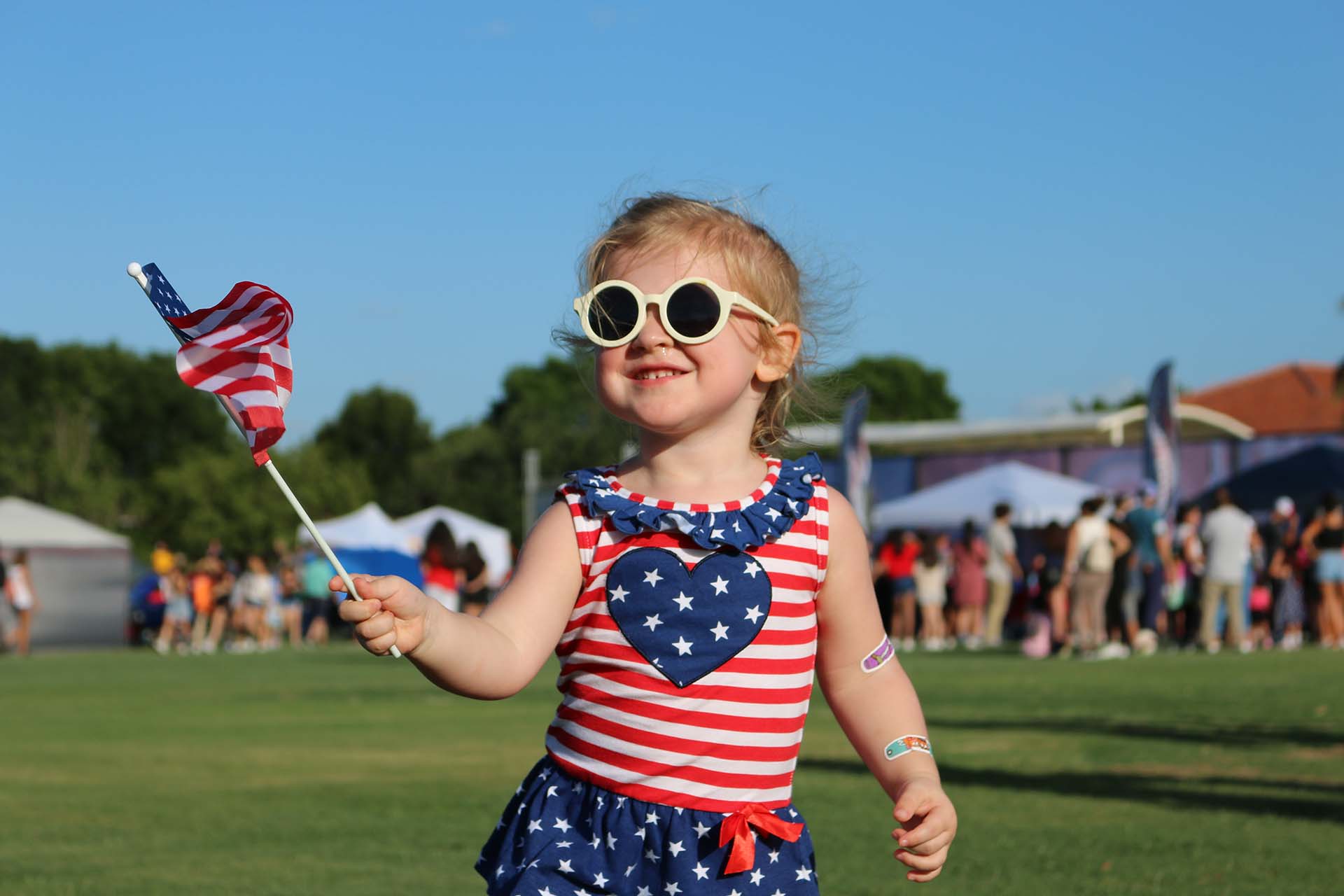 Smiling child in patriotic outfit holding an American flag at a Weston event.