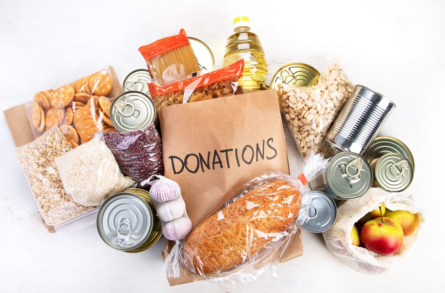 A paper grocery bag marked Donations surrounded by canned goods, pasta, cereal and bread
