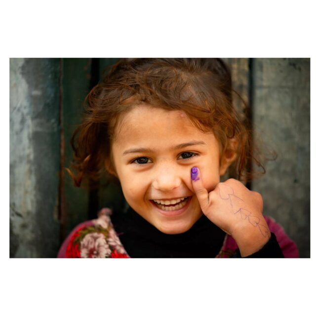 Smiling girl holding up her purple-dyed pinky finger after a polio vaccination